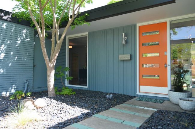 Яркая оранжевая пластиковая дверь – изюминка экстерьера частного дома, сочетающаяся с общим лаконичным дизайном